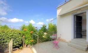 Ein Balkon mit Tisch und Stühlen, umgeben von Grünpflanzen und einem Hauseingang.