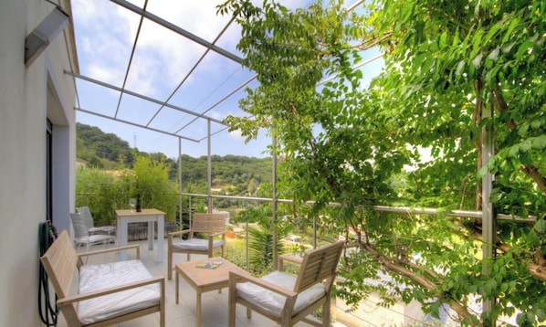 Ein Balkon mit Tisch, Stühlen und einer Hängematte, mit Blick auf eine üppige, grüne Landschaft.