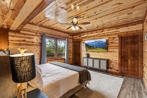 A wooden cabin bedroom with a bed, a ceiling fan, a window with a view, a mounted TV, and a cabinet. - Zennessee Luxe・IndoorPool・MtnViews・HotTub・Theater・EVCharger・PetsWelc (Sevierville)