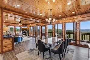 A wooden interior with a dining area, a fireplace, and large windows offering a view of the outdoors. - Zennessee Luxe・IndoorPool・MtnViews・HotTub・Theater・EVCharger・PetsWelc (Sevierville)