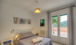 A bedroom with a bed, a bedside table, a radiator, a window with a view, and a hanging light fixture. - Amandine - BASTELICACCIA (BASTELICACCIA)