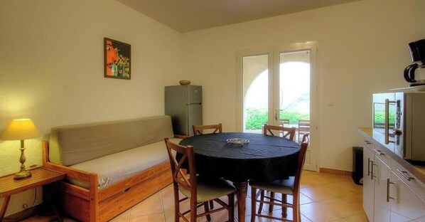 Una habitación compacta con sofá, una mesa redonda, una lámpara, refrigerador y una zona de cocina.
