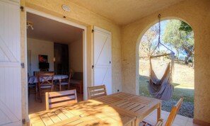 Eine offene Terrasse mit Holztisch und Stühlen, einer Hängematte und Blick ins Grüne.