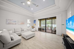 Ein modernes Wohnzimmer mit einem Ecksofa, einem Flachbildfernseher und einer großen SchiebeglasTür, die auf eine AußenTerrasse führt.