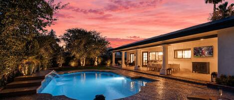 A swimming pool with a patio area, a covered outdoor seating area, and a building with large windows.