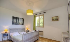 A bedroom with a bed, two bedside lamps, a window with curtains, a radiator, a painting on the wall, and a mirror. - Appulatoddiu - CANNELLE D'ORCINO (CANNELLE D'ORCINO)