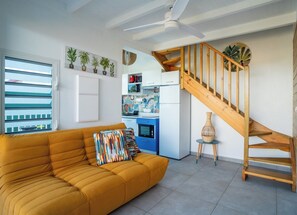 Ein modernes Wohnzimmer mit Sofa, Treppe, Küche und Blick durch ein Fenster.