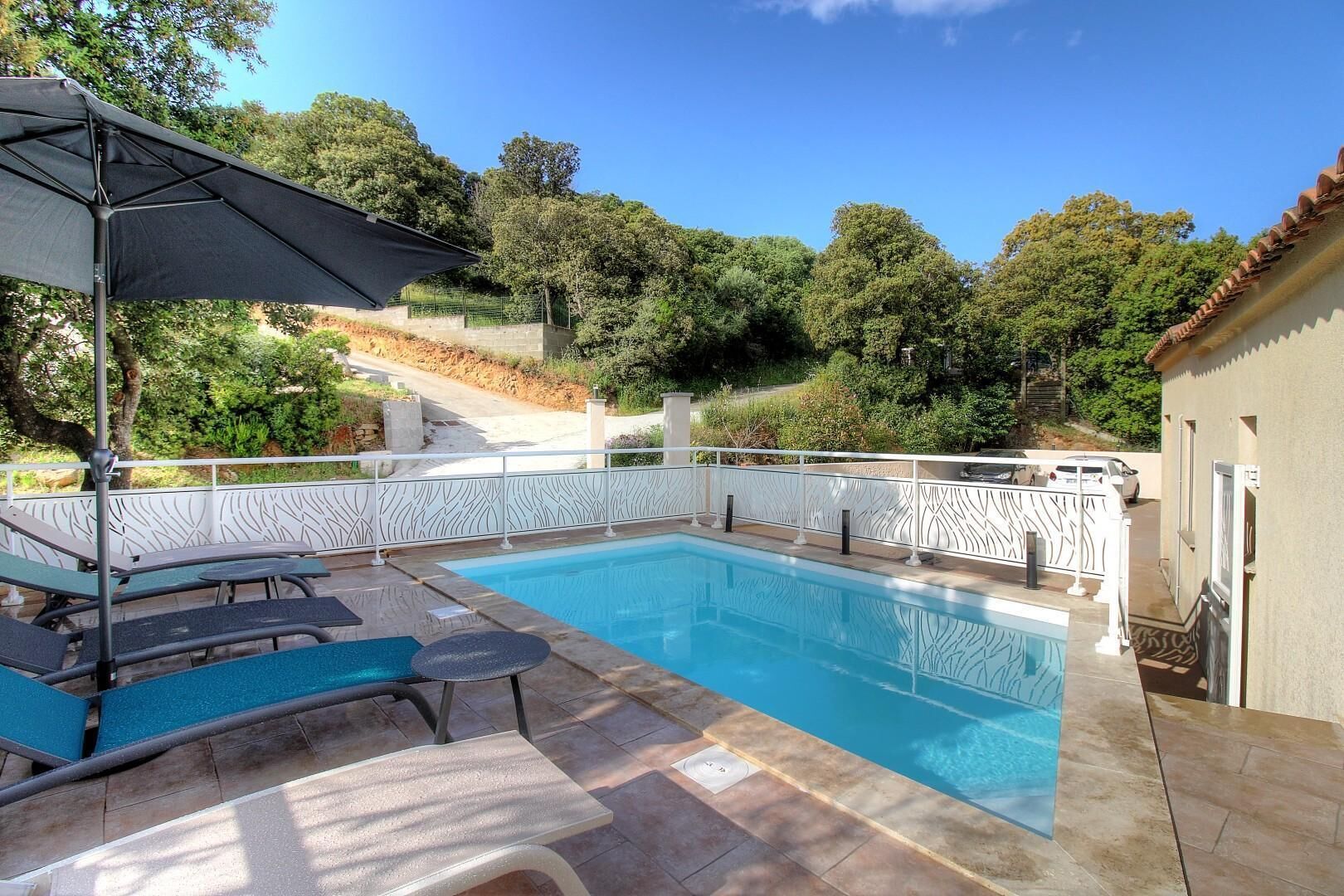 Et rektangulært swimmingpool med et hvidt dekorativt hegn, liggestole og en pergola med markise.