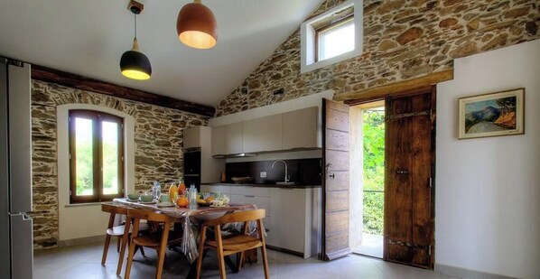 Eine rustikale Küche mit Steinwänden, Holzmöbeln und einem Essbereich mit Tisch und Stühlen.