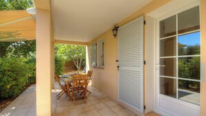 A covered patio with a table and chairs, a sliding door, and a view of the garden. - Castagnu - SANTA REPARATA DI BALAGNA (SANTA REPARATA DI BALAGNA)