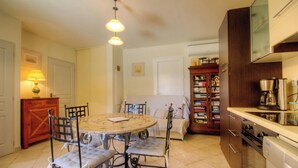 A compact kitchen with a dining table, chairs, a sofa, a bookshelf, and a coffee maker. - Castagnu - SANTA REPARATA DI BALAGNA (SANTA REPARATA DI BALAGNA)
