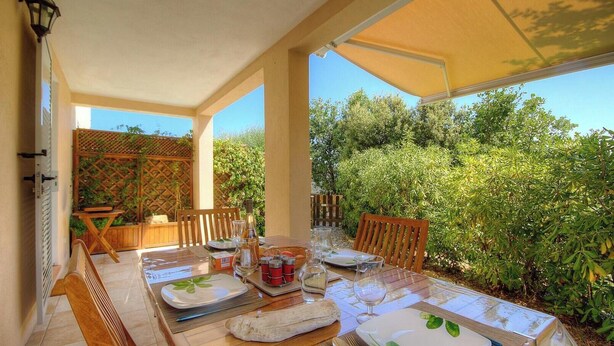 An outdoor dining area with a table set for two, surrounded by greenery and a wooden fence. - Castagnu - SANTA REPARATA DI BALAGNA (SANTA REPARATA DI BALAGNA)
