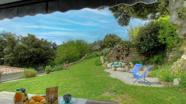 Une vue sur le jardin, avec une table dressée pour le petit-déjeuner, des sièges à l’extérieur et un mur en pierre.