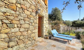 Un edificio de piedra con puerta de madera, un muro de piedra, una silla de lounge azul y un sendero de piedra.