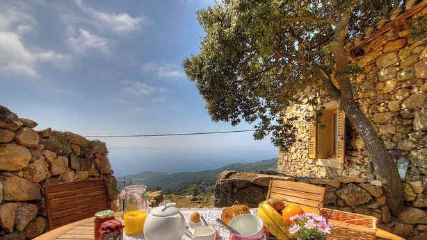 A stone building with a wooden table set for breakfast, overlooking a scenic landscape. - Casa Sola - CARGESE - Guest house (CARGESE)