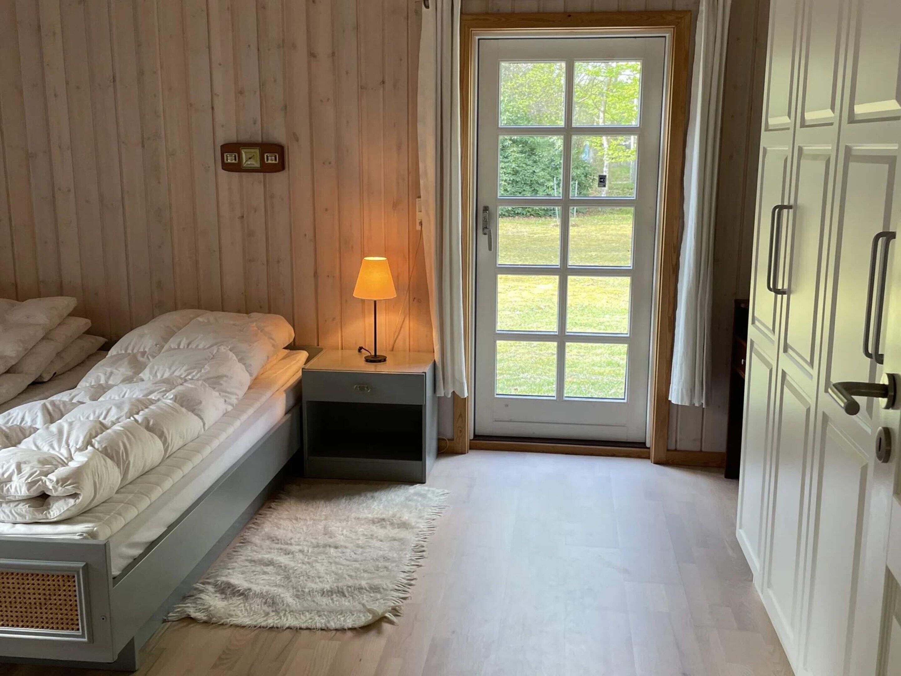 Un dormitorio con cama, mesita de noche, lámpara y puerta que da a un jardín.