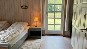 Een slaapkamer met een bed, nachtkastje, lamp en een deur naar een tuin.