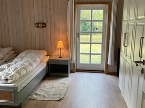 Ein Schlafzimmer mit einem Bett, einem Nachttisch, einer Lampe und einer Tür zu einem Garten.