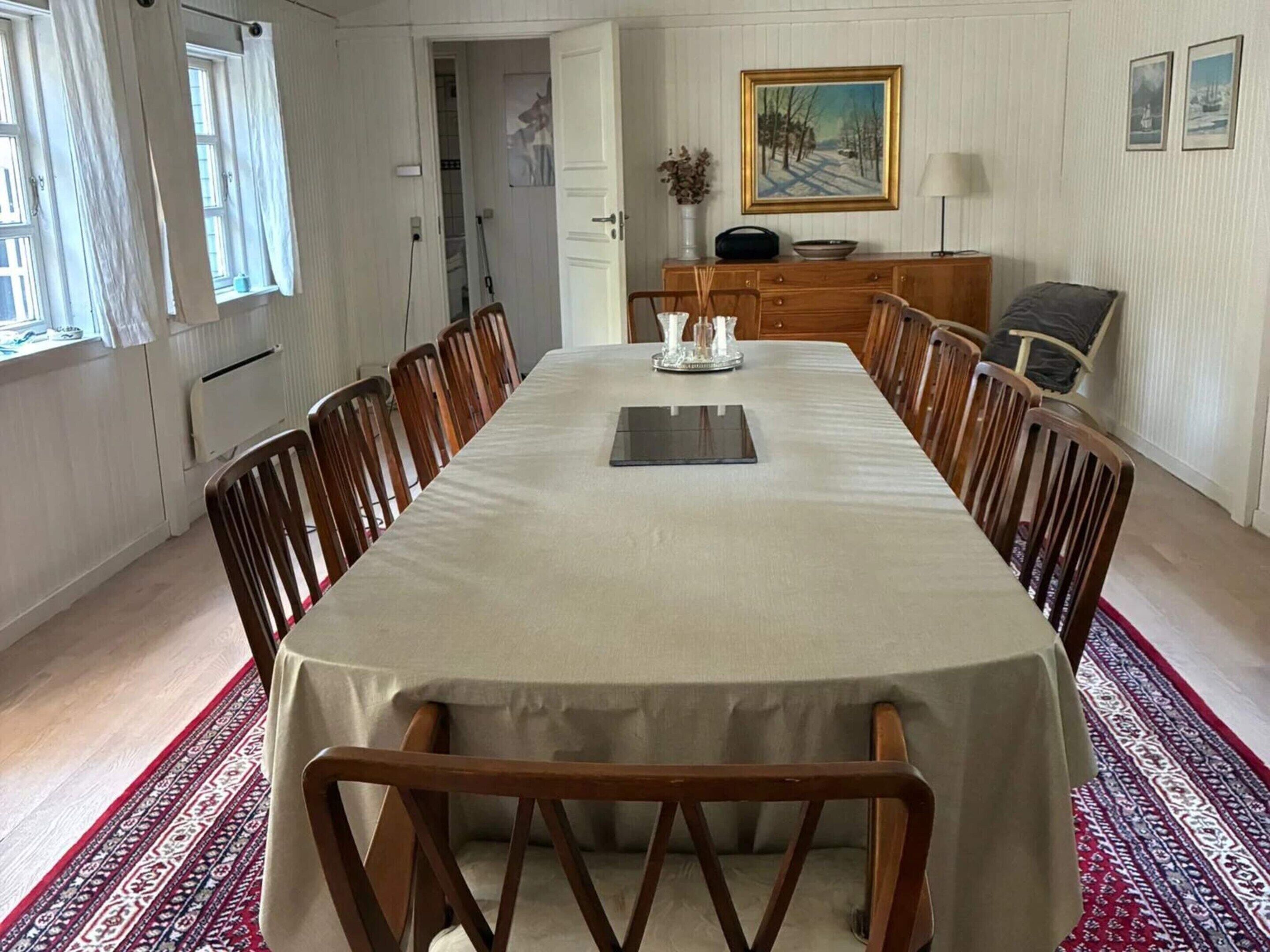 Une salle à manger avec une longue table, des chaises, un buffet et un tableau accroché au mur.