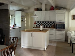 Eine Küche mit weißen Schränken, einer Holztischinsel, einer karierten Spritzschutzwand und einer hängenden Leuchte.