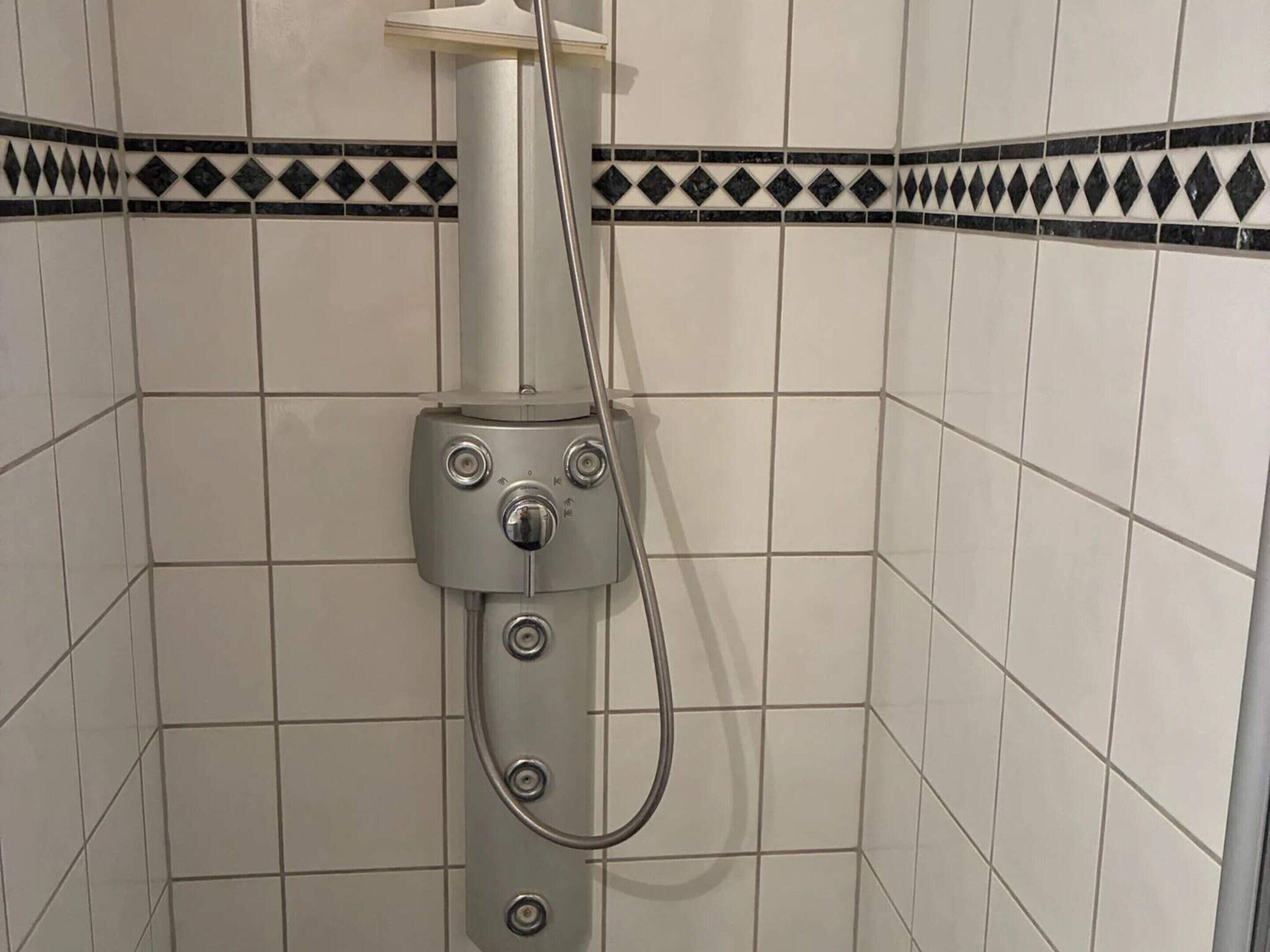 Une douche équipée d’un panneau de commande et d’un pommeau de douche amovible.