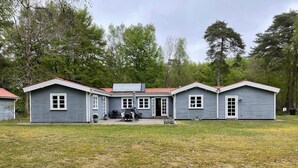Een gebouw met twee verdiepingen, een rood dak, een overdekt terras en een kleine tuin.