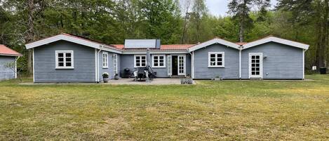 Un bâtiment à deux étages, doté d’un toit rouge, d’un patio couvert et d’un petit jardin.