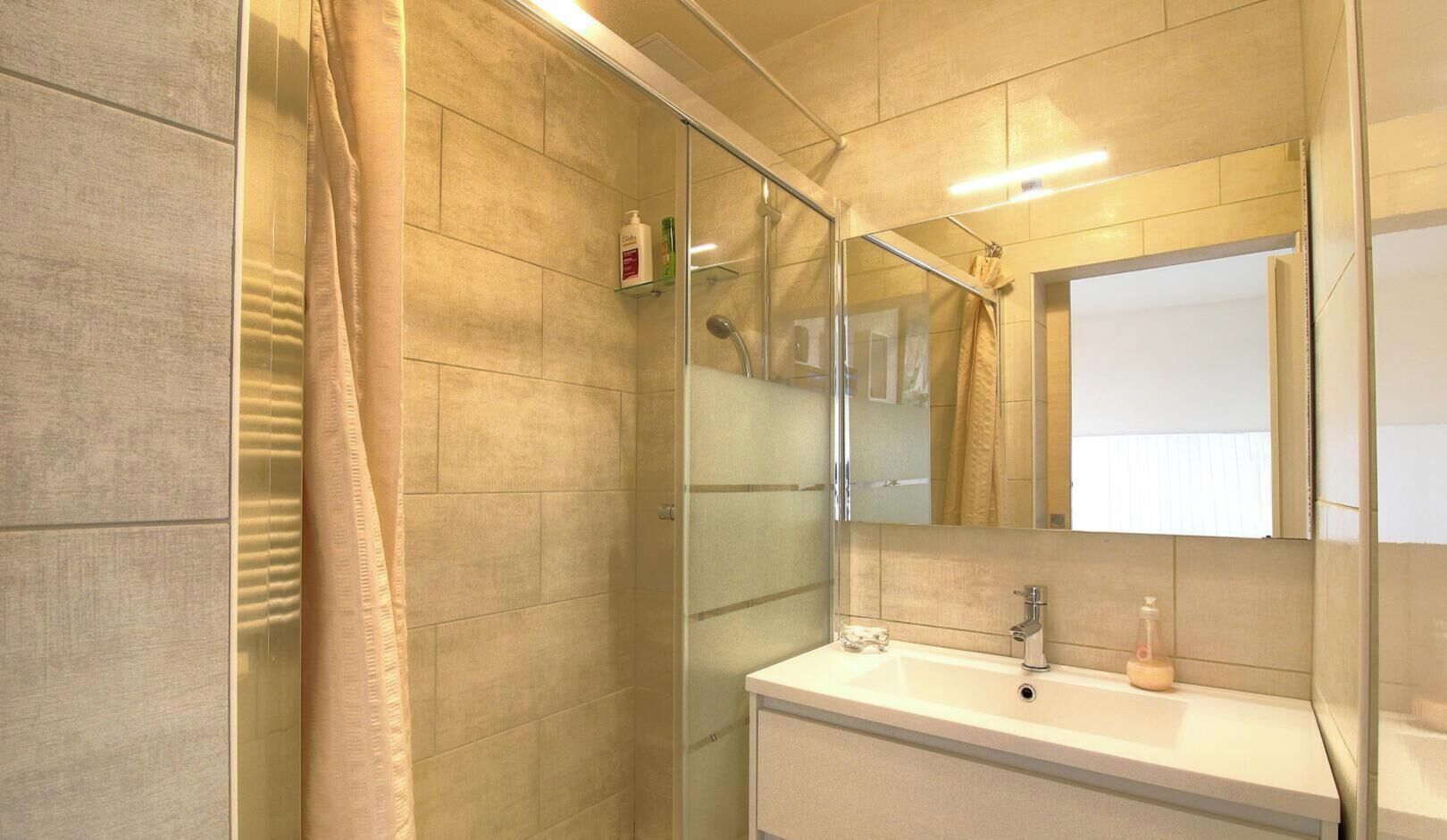 A bathroom with a glass shower enclosure, a sink with a mirror, and a towel rack.