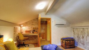 Ein gemütliches Schlafzimmer im Dachgeschoss mit schrägen Wänden, einem Holztisch, einem Stuhl, einem Bett und einem Truhenkasten.
