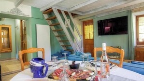 Ein Essbereich mit Tisch, gedecktem Tisch für eine Mahlzeit, einer Treppe und einem Fernseher im Hintergrund.