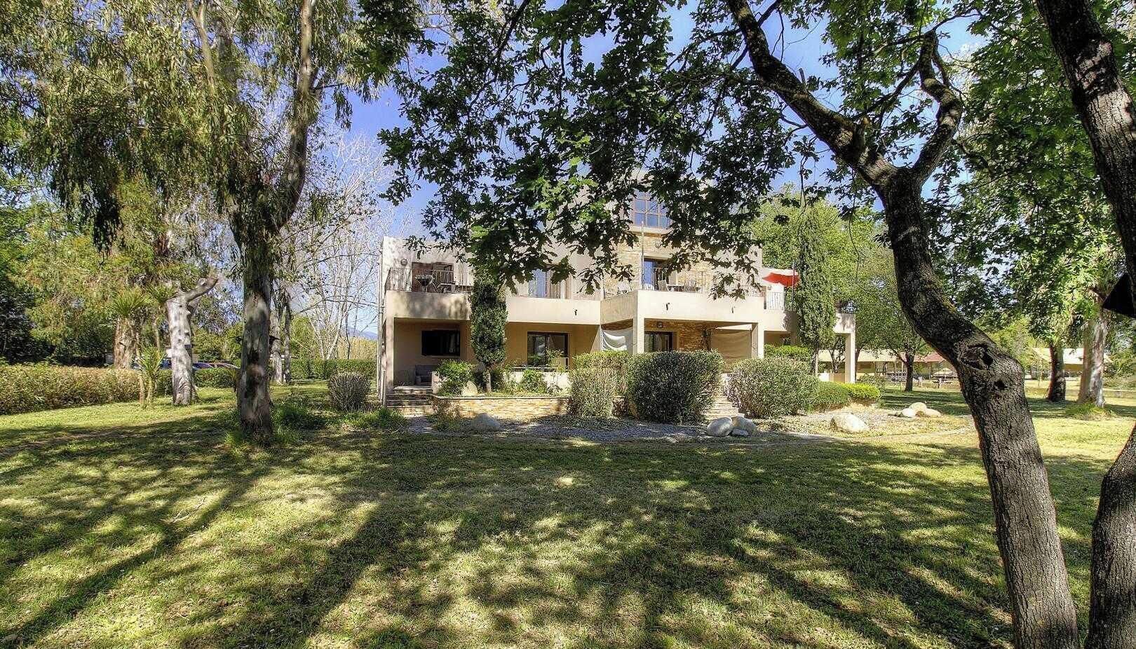 Um edifício de dois andares com varanda, rodeado por árvores e um espaço gramado.