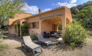 Ein Haus mit überdachter Terrasse, Sitzgelegenheit im Freien und einem Grill.