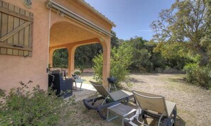 Eine Terrasse im Freien mit überdachter Sitzgelegenheit, einem Grill und einem kleinen Tisch.