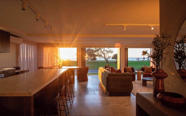 A modern kitchen with a bar area, a seating area with a sofa and chairs, and a view of the beach through large windows. - Monkirra One (Miami)