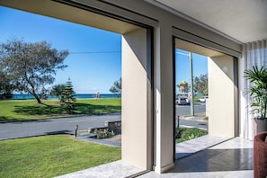A modern hotel room with a large sliding glass door leading to a balcony with a view of the sea and a grassy area. - Monkirra One (Miami)