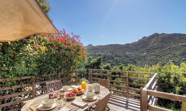 Eine Holzterrasse mit Frühstückstisch, mit Blick auf eine gebirgige Landschaft.