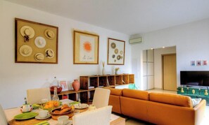 Ein Wohnzimmer mit einer Couch, einem Esstisch mit einer Vase und einem Fernseher.