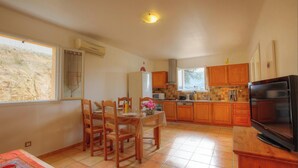 A compact kitchen with wooden cabinets, a dining table with chairs, a TV, and a window with a view of the outside. - L'oliveraie 2 - SOLLACARO (SOLLACARO)