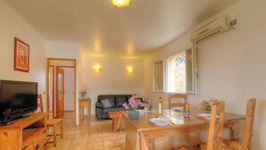 A living room with a TV, sofa, dining table, chairs, and a window. - L'oliveraie 2 - SOLLACARO (SOLLACARO)