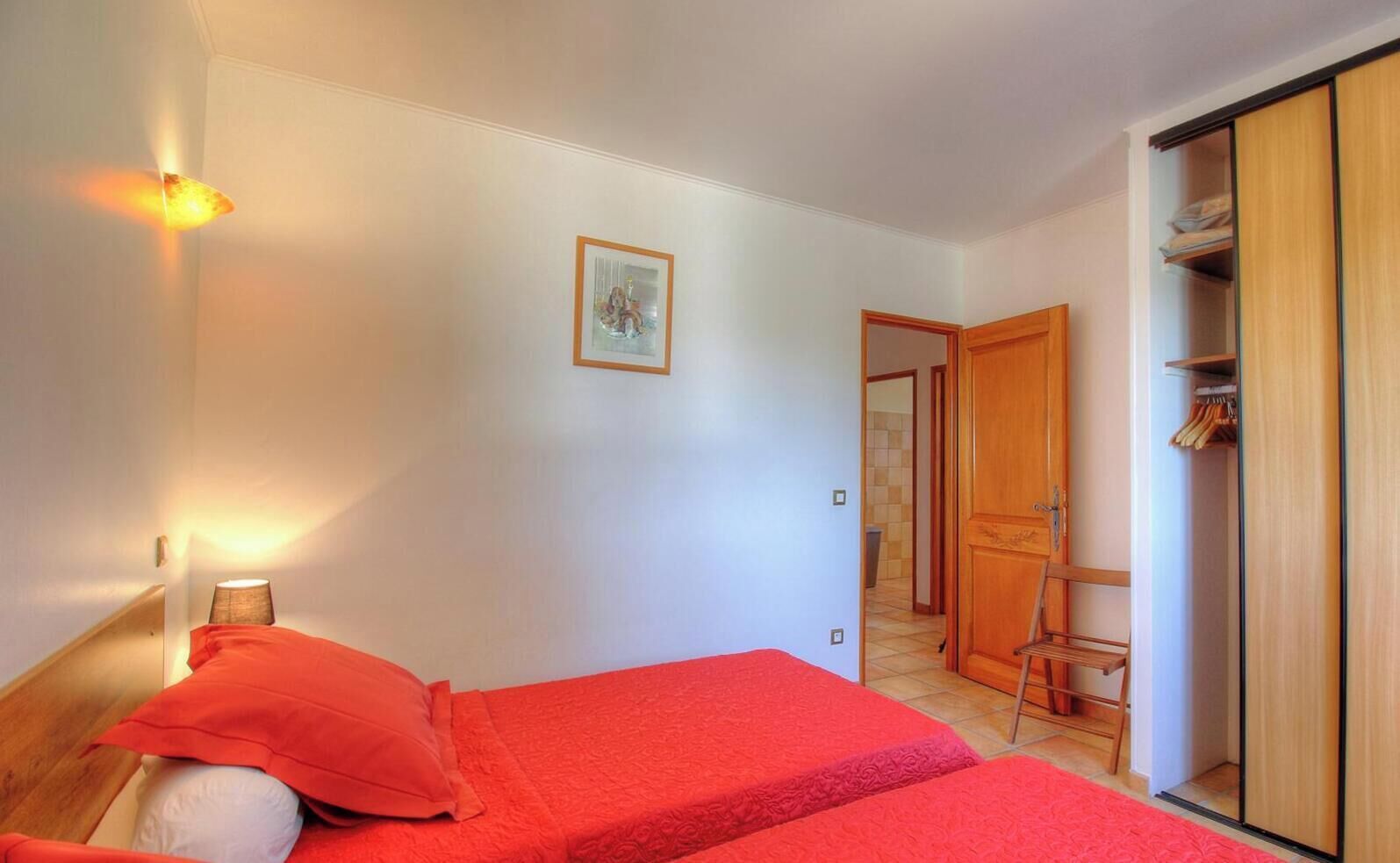 Ein Schlafzimmer mit zwei Betten, einem Kleiderschrank, einem Schreibtisch und einer Tür zu einem weiteren Raum.