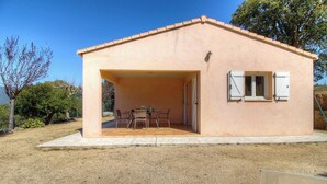 A single-story building with a covered patio area, a table and chairs, and a window with shutters. - L'oliveraie 2 - SOLLACARO (SOLLACARO)
