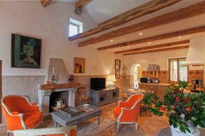Ein gemütliches Wohnzimmer mit Kamin, orangefarbenen Sesseln, einem Fernseher und einer Küchenzeile mit Mikrowelle.