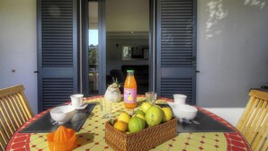 Una mesa con una cesta de frutas, un vaso de zumo de naranja y una jarrón.