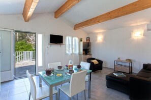 Ein modernes Wohnzimmer mit einem Glastisch, weißen Stühlen, einem schwarzen Sofa und einem an der Wand befestigten Fernseher.