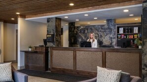 Een receptiegedeelte met een houten plafond, een stenen muur en een balie met een computer. Er staan twee banken en een salontafel.