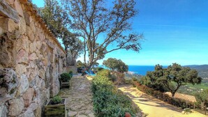Un camino de piedra que lleva a una terraza con vistas al mar y al paisaje distante.