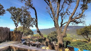 Una terraza de madera con una mesa y sillas, rodeada de árboles y vistas a un valle.