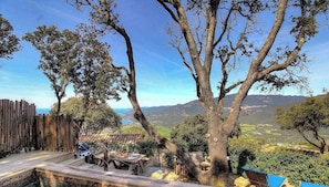 Una terraza de madera con una mesa y sillas, rodeada de árboles y vistas a un valle.