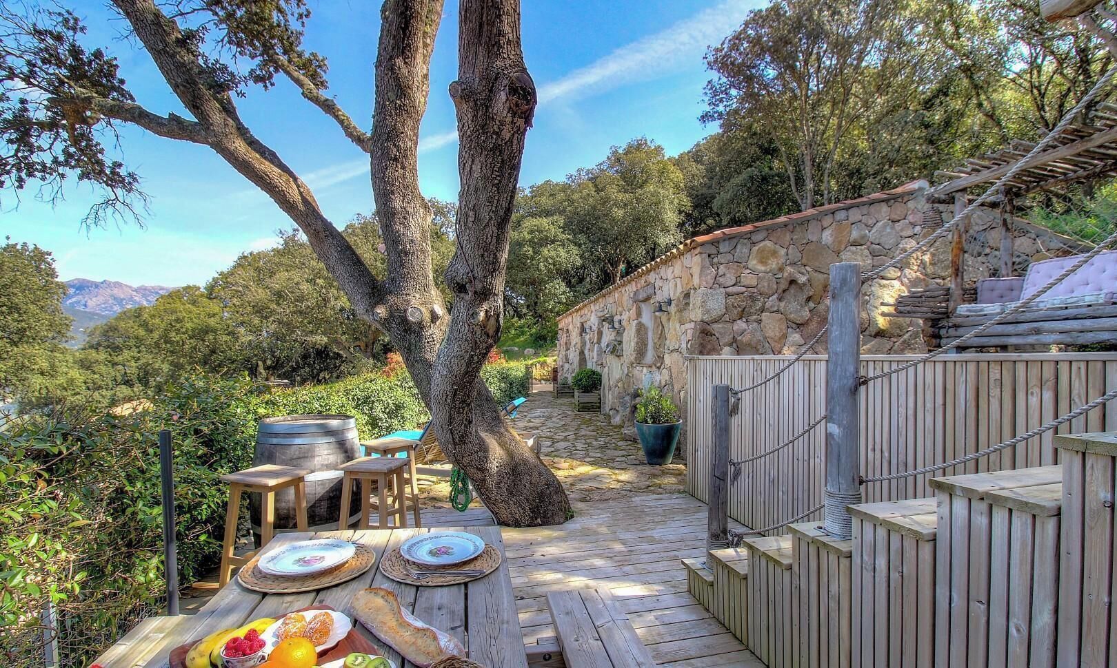Une terrasse en bois avec des meubles d’extérieur, un mur en pierre et un arbre.