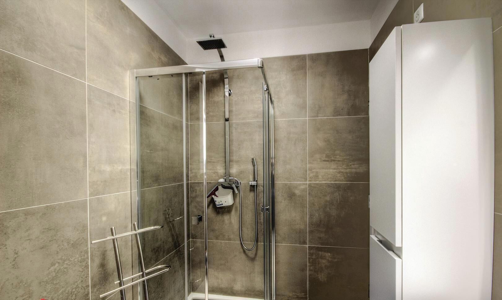 Een douche met een glazen deur, een handdouche en een wandmengkraan.